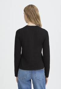 Črn pulover z dolgimi rokavi, okrogel izrez in prilegajoč kroj. Gladek tekstura, združena z modrimi kavbojkami z visokim pasom.
