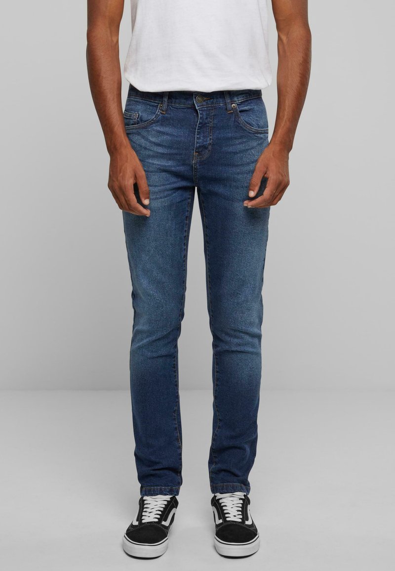 Jeanși din denim albastru cu croială slim, design cu cinci buzunare și o ușoară decolorare. Asociați cu adidași din pânză alb-negru.