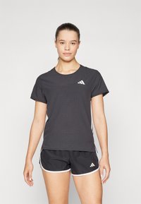 Svart atletisk t-skjorte med korte ermer og perforert tekstur, med en hvit Adidas-logo på brystet. Kombinert med svarte shorts.