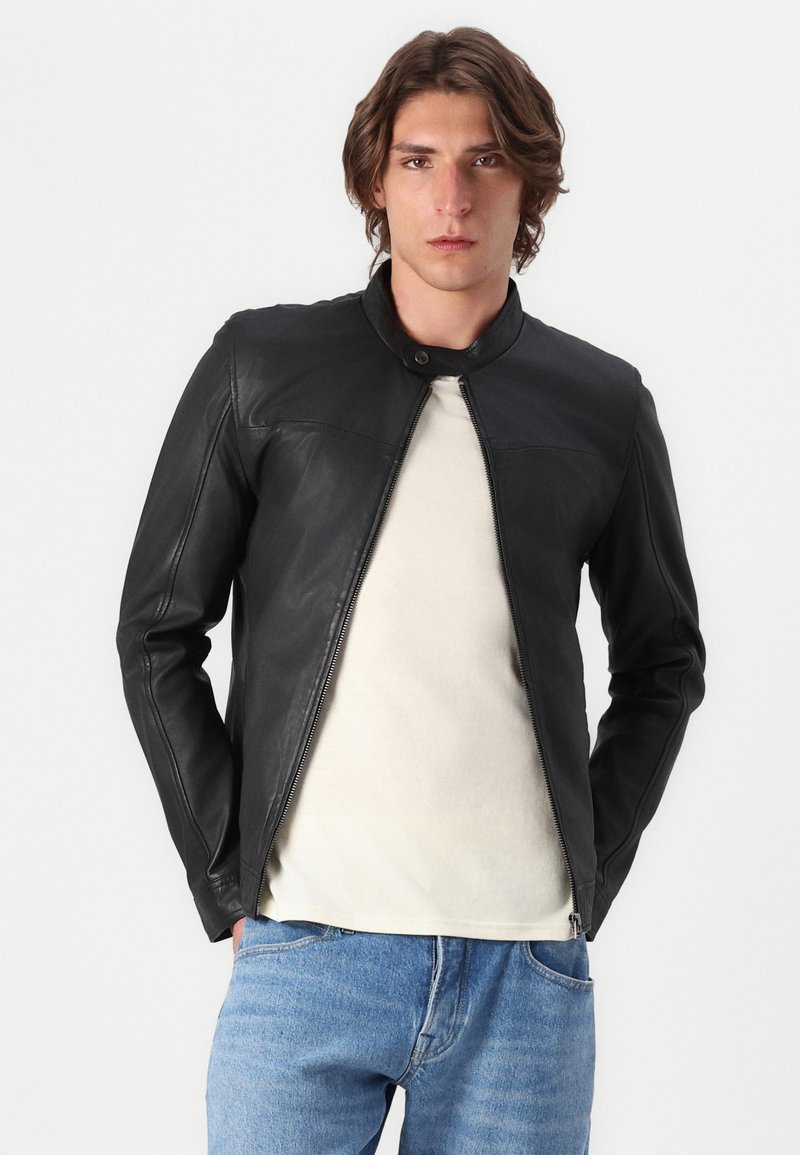 Schwarze Lederjacke mit hohem Kragen, vorderem Reißverschluss und glatter Textur. Trägt man über einem hellen T-Shirt und blauen Denim-Jeans.
