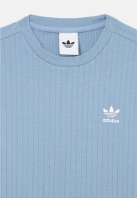 T-shirt bleu clair à rayures, à manches courtes, avec un col rond et un logo Adidas blanc sur la partie gauche de la poitrine. Texture douce.