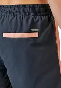 Shorts noirs avec une taille élastique, présentant une poche horizontale rose à l'arrière et une petite étiquette de logo adjacente à la poche.