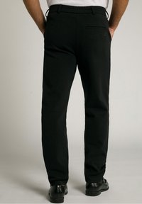 Svarta byxor med en slät yta, med ett resårmidjeband och en bakficka. Modellen bär svarta skor.