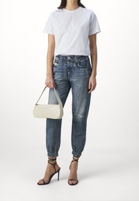 Witte t-shirt met korte mouwen, verwoeste lichtblauwe denim joggers, zwarte strappy hoge hakken, en een kleine off-white handtas.