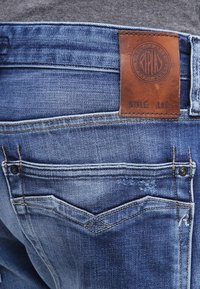 Denimjeans med en klassisk blå tvätt, med en brun läderetikett vid midjan och bakfickor med en sydd design.