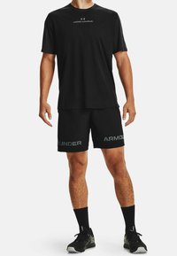 Svart idrottsklädsel bestående av en kortärmad tröja med "Under Armour"-logotyp, svarta shorts med grå branding, i kombination med svarta strumpor och skor.