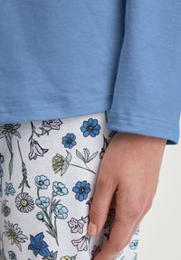 Lichtblauw langemouwen shirt met een gladde textuur, gecombineerd met witte broek met een multikleurige bloemenprint.