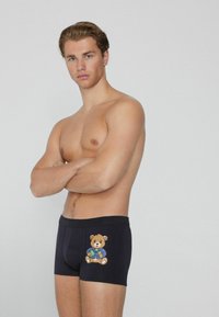 Pánské černé boxerky vyrobené z elastického materiálu, s barevným motivem medvěda na levé noze. Hladká textura a přiléhavý střih.