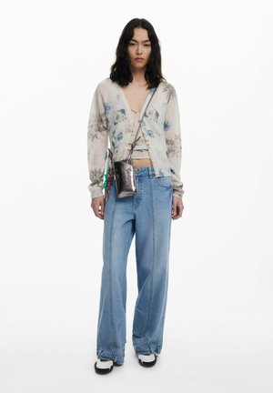 Cardigan a maglia con motivo floreale, beige chiaro con accenti blu, abbinato a pantaloni in denim blu chiaro a vita alta. Borsa a tracolla in argento.