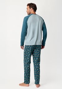 Camisa de pijama de manga larga en color verde azulado y azul claro, combinada con pantalones estampados que presentan pequeños diseños de perros sobre un fondo verde azulado.