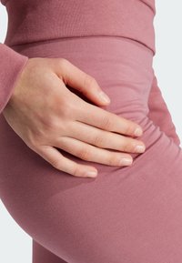 Tejido rosa acanalado con un diseño ajustado. Una mano descansa sobre la cintura, enfatizando la textura suave y los contornos de la prenda.