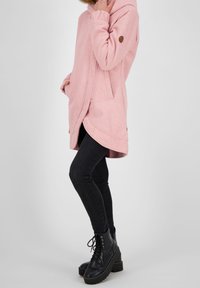 Hoodie rosa con cappuccio, tasche laterali e orlo curvo. Realizzato in tessuto morbido, presenta una toppa con logo marrone sulla manica e una vestibilità rilassata.