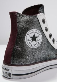 Vysoké tenisky Converse s černým třpytivým svrškem, bordó semišovou patou, bílými průchody pro šňůrky a kruhovou nášivkou s logem na boku.