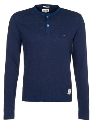 Marineblå langærmet Henley-skjorte med to knapper, lille logo på venstre bryst og påsyet label nær nederste kant.