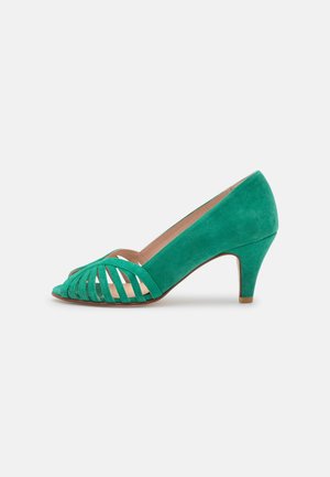 Tacones de ante verde con punta descubierta y diseño ranurado en la parte delantera, con una altura de tacón moderada, que presentan una textura suave y una silueta curvada.