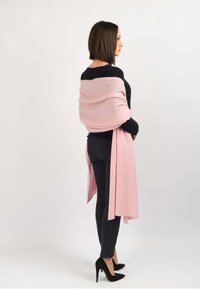 Lyserød cashmere sjal draperet over skuldrene, stylet med en sort top og tætsiddende sorte bukser, der har elegante sorte højhælede sko.