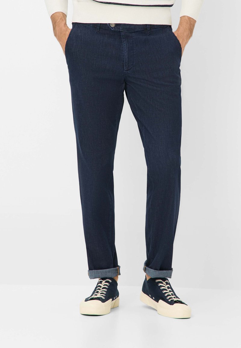 Pantaloni in denim blu navy con taglio dritto, caratterizzati da orli arrotolati e una superficie testurizzata. Abbinati a sneakers blu navy e a un maglione crema.