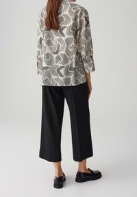Blouse ample présentant un motif ondulé noir et blanc, associée à un pantalon large noir et des chaussures slip-on noires.