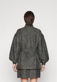 Black and silver textured jacket with a belted waist, dropped shoulders, and a high collar, featuring a layered back design.