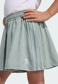 Light green athletic skirt with textured dots, elastic waistband, and three vertical stripes. Features a silver Adidas logo.