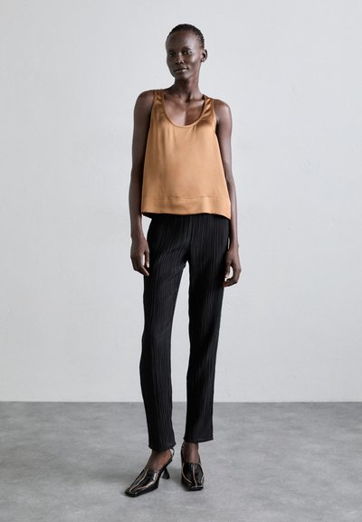 Top senza maniche in satin bronzo abbinato a pantaloni neri a righe. Il modello indossa mule nere con tacco. Design semplice e moderno con linee pulite.