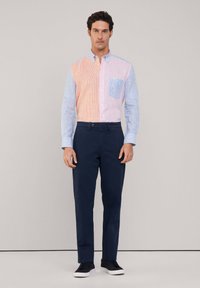 Camisa de botones con secciones de rayas en tonos pastel rosa y azul alternando, un bolsillo, combinada con unos pantalones oscuros de color marino y zapatillas negras.