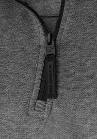 Šedý zip-up top vyrobený z texturované tkaniny, s černým zipem, na kterém je značka "STREET ONE" a nápis "SEEK ADVENTURE" na poutku.