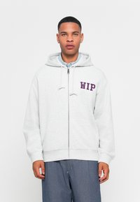 Gray zip-up hoodie with a drawstring and purple "WIP" text on the left chest. Soft cotton material, relaxed fit, and front pockets.