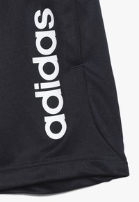 Navy šortky s texturovanou tkaninou, zdobené výrazným bílým logem "adidas" potištěným na straně a jedním detailem kapsy.