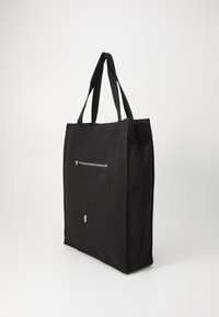 Black canvas tote bag with dual handles, front zipper pocket, and a simple logo accent. Features a rectangular shape and textured fabric.