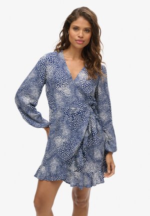 Vestido envolvente de estampado azul y blanco con mangas largas, escote en V, fruncido en la cintura y un dobladillo con volantes. Tejido ligero con textura punteada.