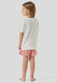T-shirt en coton blanc à manches courtes, associé à un short rayé multicolore avec un ourlet volé. L'enfant est pieds nus.