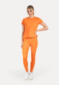 Top deportivo naranja combinado con leggings a juego. Ambas prendas están hechas de una tela lisa y elástica, con un diseño sencillo y ajustado.