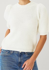 Maglione bianco lavorato a maglia con un motivo testurizzato, scollo rotondo e maniche corte svasate. Abbinato a jeans in denim blu.