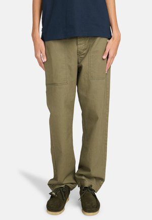 Olive green, loose-fitting cargo pants with double front pockets, stitched detailing, and a straight cut. Worn with brown suede shoes.