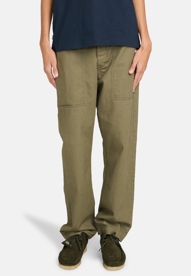 Pantaloni cargo verde oliva, morbidi e larghi, con doppie tasche frontali, dettagli cuciti e taglio dritto. Indossati con scarpe in suede marroni.