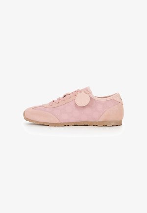 Sneaker bassa rosa con motivo a pois, chiusura con lacci sul davanti, suola in gomma e un'etichetta decorativa rotonda vicino ai lacci su sfondo bianco.