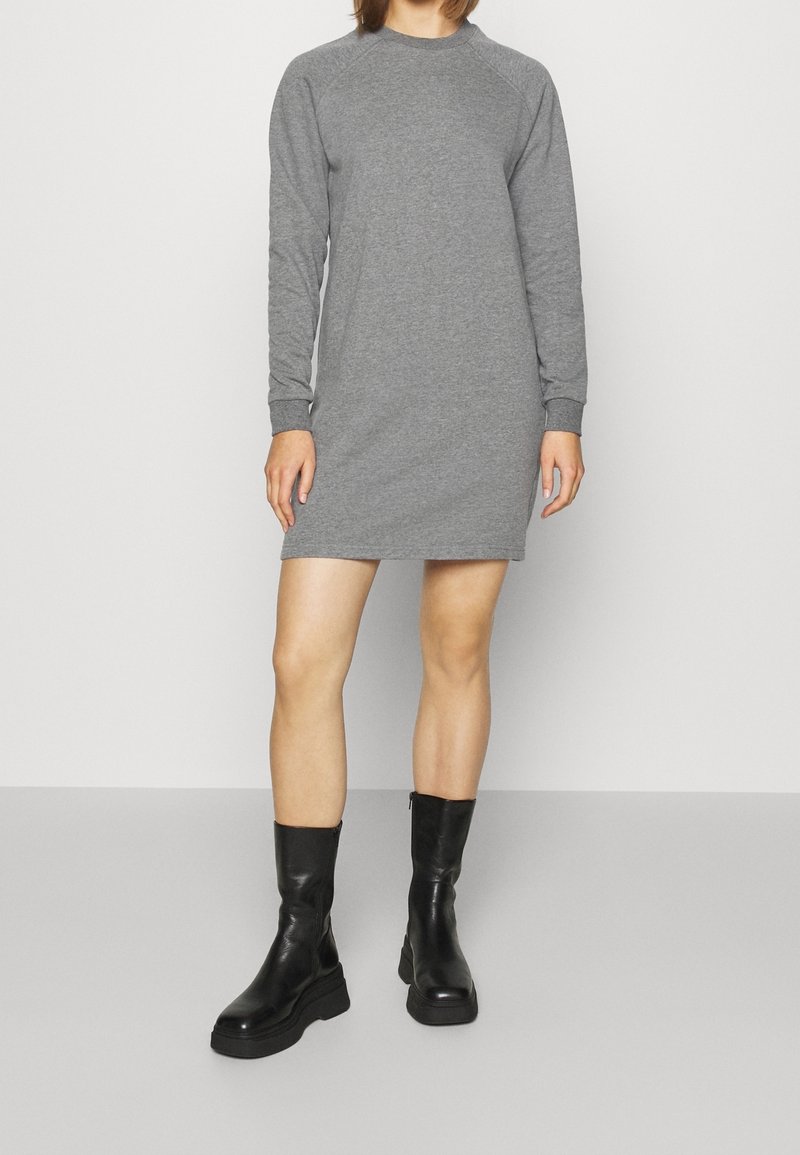 Vestido gris de manga larga en un tejido suave con escote redondeado y puños acanalados, combinado con botines negros hasta el tobillo con suela gruesa.