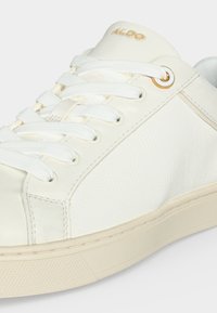Baskets en cuir blanc avec lacets blancs, semelle beige, œillet en métal doré et logo ALDO doré sur la languette rembourrée.