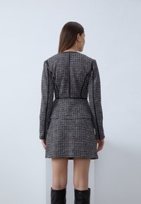 Černobílé tweedové šaty s přiléhavým siluetou, dlouhými rukávy a koženými detaily na ramenou a švech.