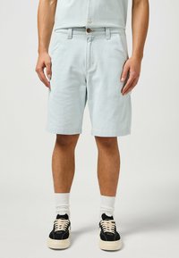 Pantalones cortos de rayas azul claro, hechos de algodón, con cierre de botones, bolsillos laterales y un ajuste relajado, combinados con zapatillas negras y calcetines blancos.