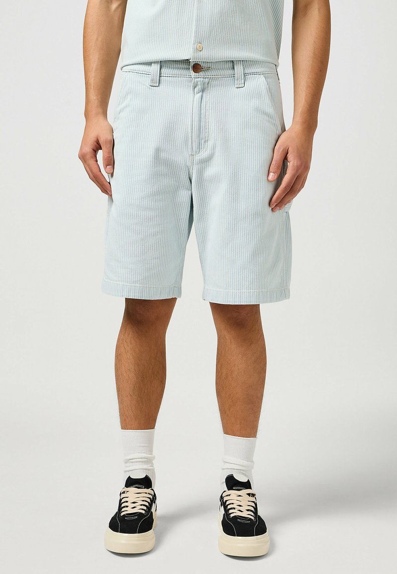 Pantalones cortos de rayas azul claro, hechos de algodón, con cierre de botones, bolsillos laterales y un ajuste relajado, combinados con zapatillas negras y calcetines blancos.