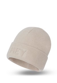 Beige gebreide muts met een omgeslagen rand, voorzien van de tekst "HEY" in reliëf aan de voorkant. Zachte textuur en ronde vorm, geschikt voor casual kleding.