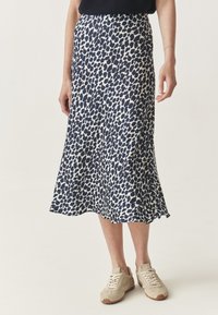 Hame midi dengan motif leopard biru laut dan putih dengan siluet mengalir, terbuat dari bahan ringan, dilengkapi dengan belahan samping dan dipadukan dengan sepatu sneakers beige.