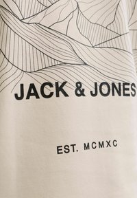 T-shirt en coton blanc avec un art linéaire noir représentant des vagues abstraites et du texte : "JACK & JONES" et "EST. MCMXC" en lettres grasses.