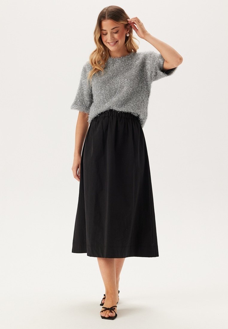 Grijze fuzzy shirt met korte mouwen, gecombineerd met een zwarte, taille-elastische rok tot de enkels. Gecompleteerd met zwarte sandalen met strikdetails.