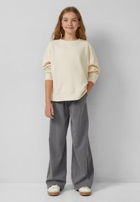 Felpa oversize di un beige chiaro con spalle scese, abbinata a pantaloni grigi a gamba larga e sneakers bianche con suole color nocciola.