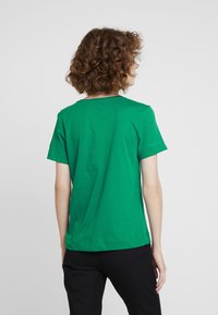 Camiseta de algodón verde de manga corta con cuello redondo clásico y diseño de hombros sin costuras, mostrada desde atrás sobre un fondo neutro.