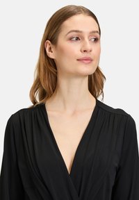 Abito avvolgente nero con scollatura a V profonda, maniche lunghe e spalle plissettate. Tessuto morbido e fluido con dettagli di design minimalisti.