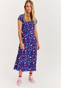 Modrá květinová šaty s krátkými rukávy, se živými vzory listů a ovoce. V doprovodu růžových tenisek pro kontrast.